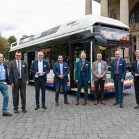 Acht Personen stehen vor einem Wasserstoffbus vor dem Wiesbadener Kurhaus