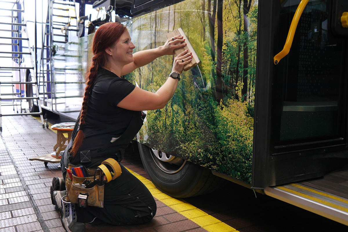 Werbemitteltechnikerin beklebt Bus mit Werbung