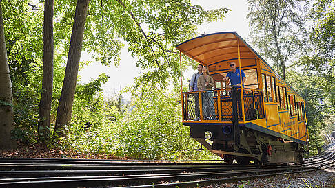 Seitliche Ansicht: Zwei Fahrgäste mit ESWE Mitarbeiter im Nerobergbahn-Waggon während der Fahrt